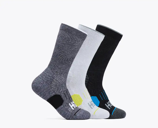 A pack of three Hoka Crew Run Socks in a 3-color assortment, featuring light grey, dark grey, and black. The socks display various designs including a patterned design on the dark grey pair and a 'Time to Fly' text on the interior opening of the light grey pair.
