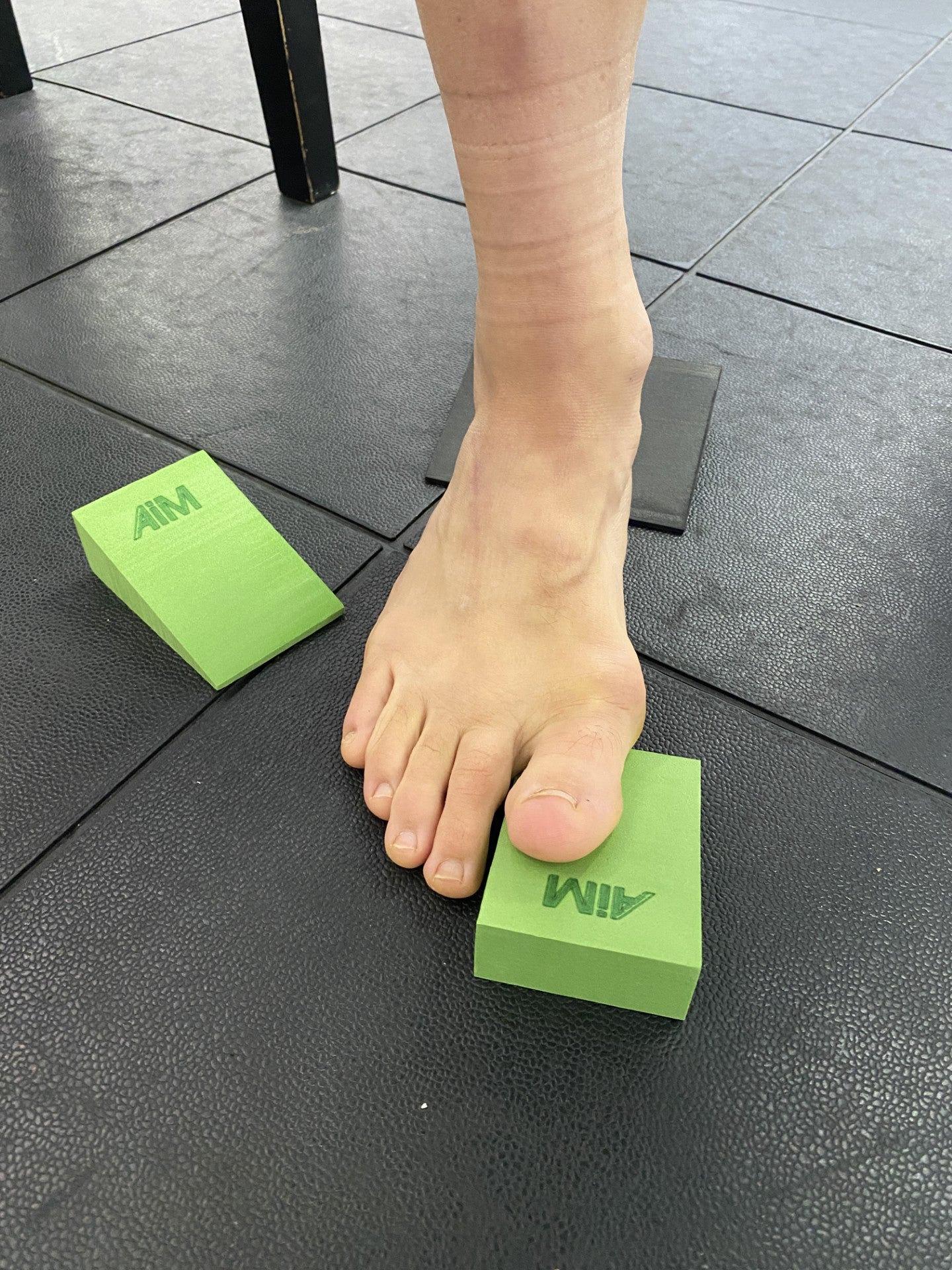 Person using green foam wedges on a black tiled floor
