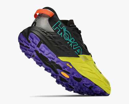 A Hoka Men's Speedgoat 7 trail running shoe in black, purple, and neon yellow, shown from a three-quarters angle against a light gray background.