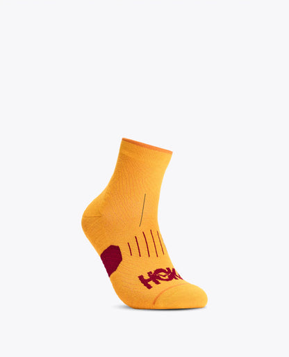 A single low-cut athletic sock in bright yellow with a dark red heel accent and the HOKA logo printed on the toe, shown against a plain white background.