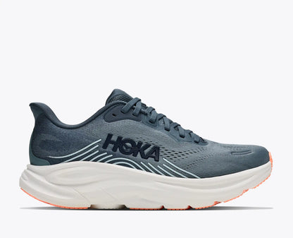 A HOKA running shoe in slate blue-gray with a thick white midsole and orange outsole accents, shown from a side profile on a light gray background.