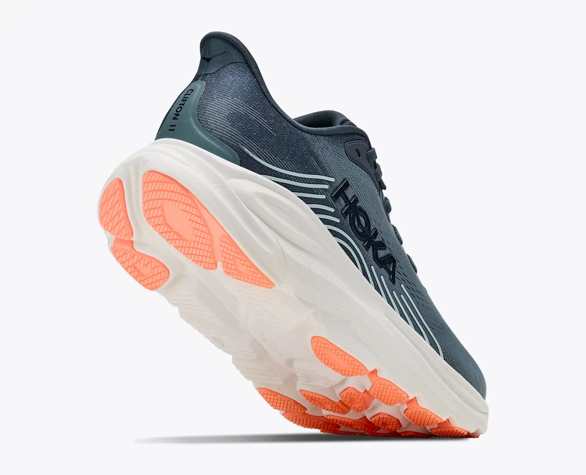 A Hoka running shoe in dark slate blue and white with vibrant orange accents on the sole, shown from a dynamic three-quarters angle against a light gray background.