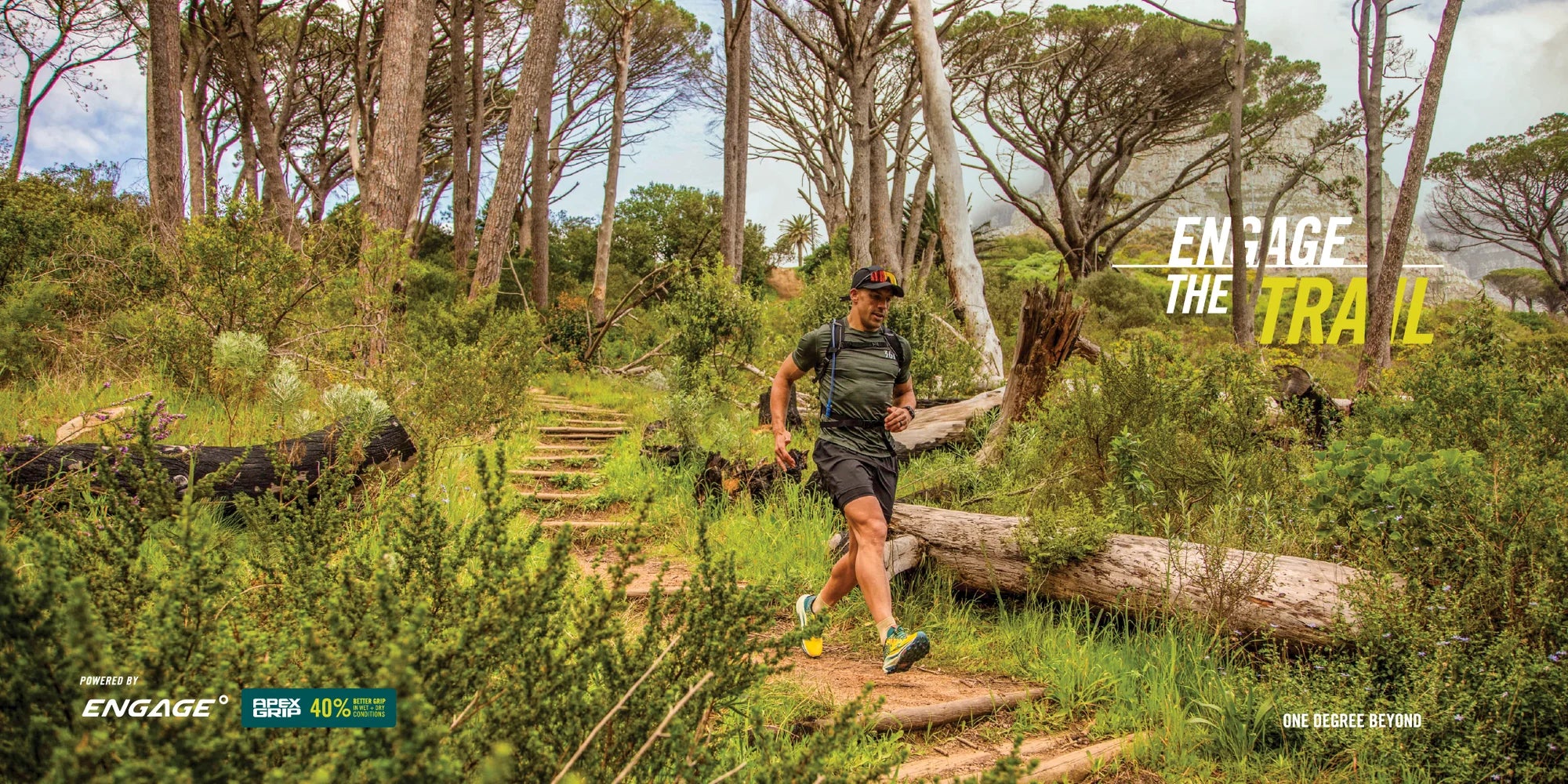 A trail runner wearing a black athletic outfit and running shoes moves along a wooden boardwalk path through a dense green forest with trees and logs. Large text on the right reads 'ENGAGE THE TRAIL', and small ENGAGE branding appears at the bottom left.