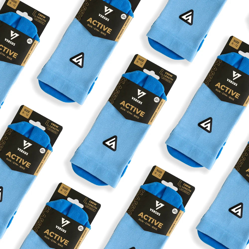 Light blue crew socks with bright blue tips, packaged in black and gold Vessel brand cards, arranged diagonally on a white background.