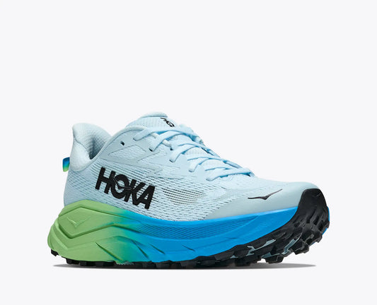 A HOKA Challenger trail running shoe in light blue with a black logo, a bright blue midsole, and a green-to-yellow gradient near the front, shown on a light gray background.