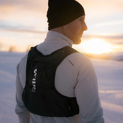Person with a black backpack standing in a snowy landscape at sunset