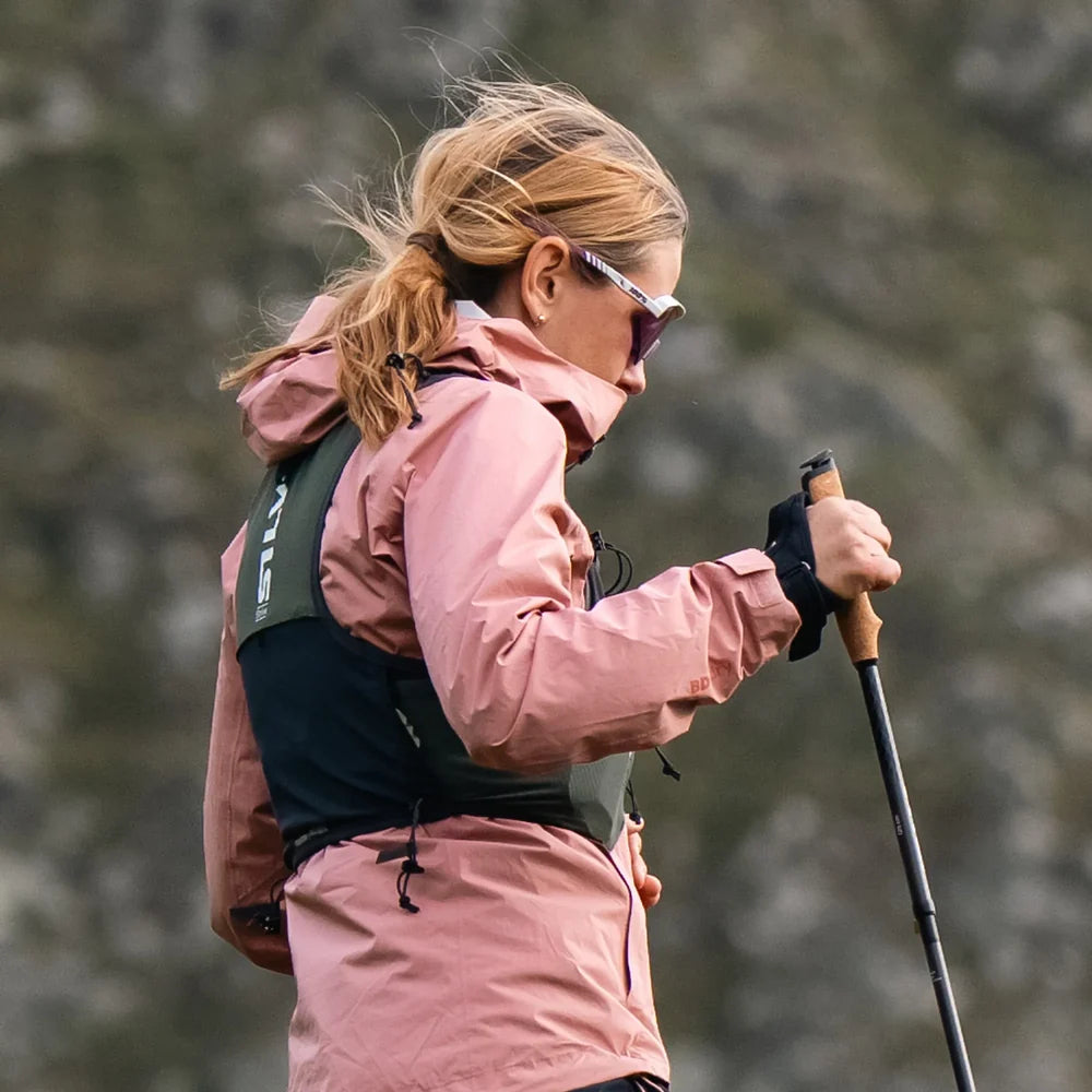 Woman in pink jacket with hiking poles and running vest in a forest setting