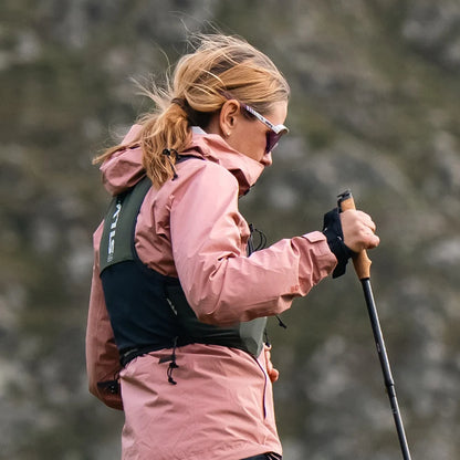 Woman in pink jacket with hiking poles and running vest in a forest setting