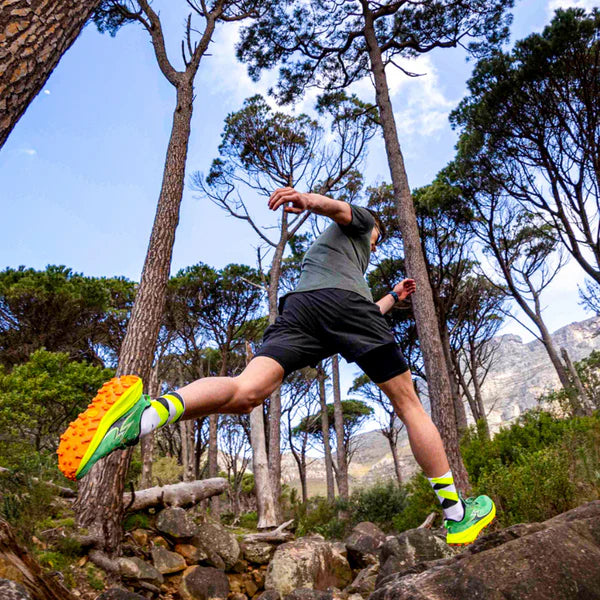 Person running on a rocky trail in a forest with mountains in the background