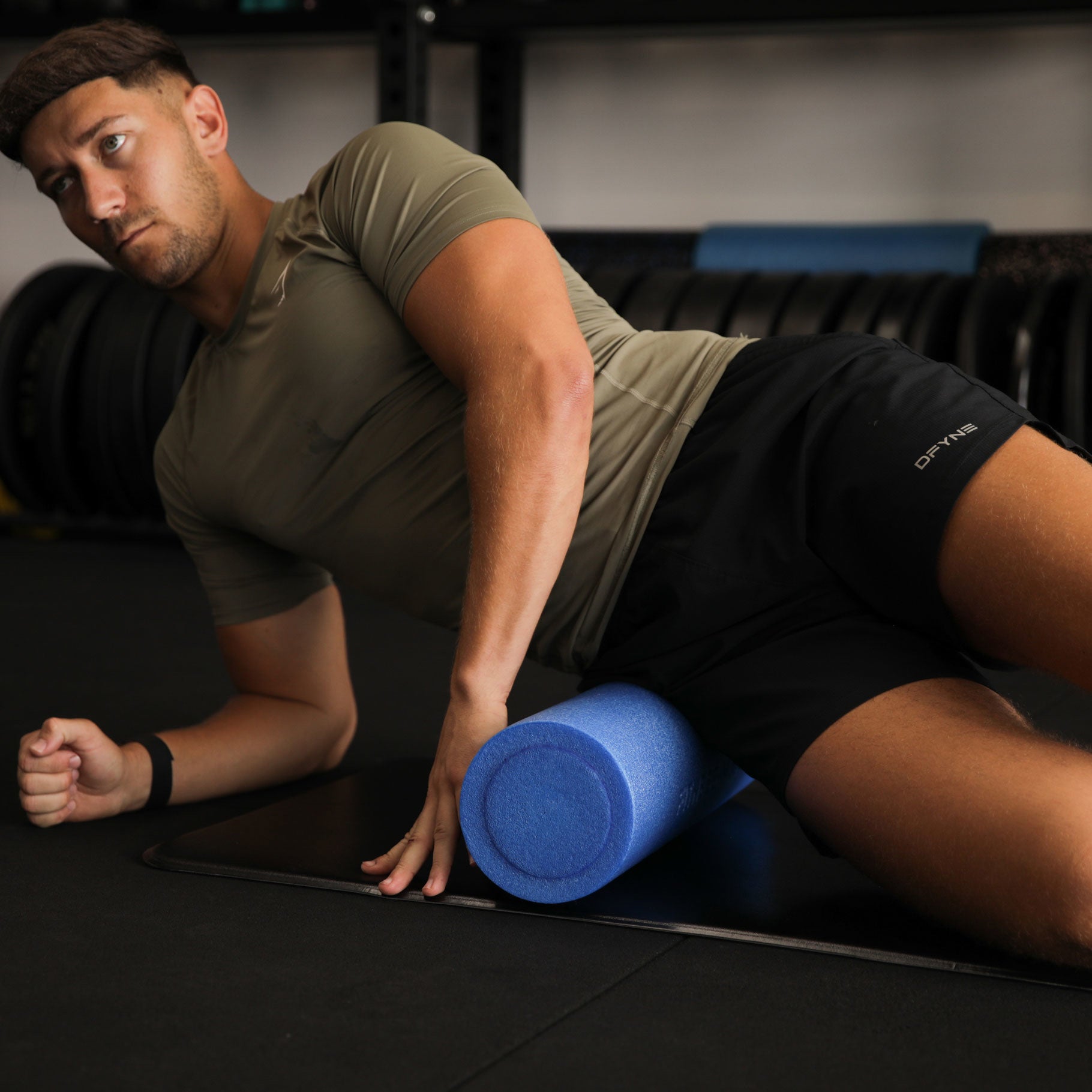 Man using a blue foam roller on a black mat in a gym setting
