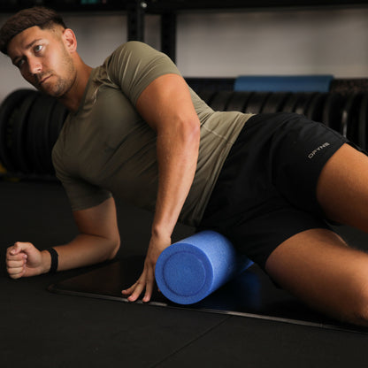 Man using a blue foam roller on a black mat in a gym setting